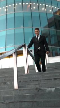 Genç başarılı iş adamı kolay slayt üzerinde açık merdivenler demiryolu ile gülümseme ve atlama vasıl belgili tanımlık son. Bina arka plan cam iş merkezi. Deniz mavisi ve turuncu tarzı. Geniş Ultra Hd tripod vurdu