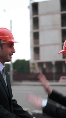 4 bin. UltraHD. Takım elbiseli iki işadamı mimar, kasklarına vurmaktansa iki koluna da beşlik çakıyor. Projeyi bitirdikleri için çok mutlu görünüyorlar. İş konseptindeki deliler. Dikey Çekim.