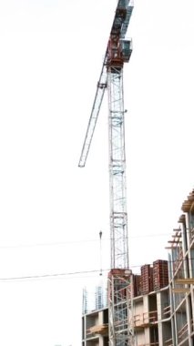 4 bin. Mobil vinç beton kirişi montaja taşır. İşçiler sahaya yardım ediyor. Yeni inşa edilmiş deniz mavisi ve turuncu nesnelerin geniş açılı görüntüsü. Çeviriyorum. Dikey Çekim.