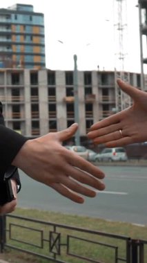 Ağır çekim. El sıkışan iki genç başarılı iş adamları. Kask ile metin yastık, takım elbise ve kravat müşteri içinde architector. yapım aşamasında vinç ve kirişler bg. ile bina orta vurdu