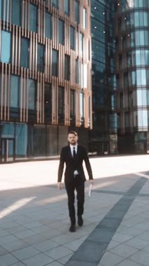 4 k. Pov. Sakal ve bıyık kameraya, textpad yolda belgelerle elbiseli genç başarılı iş adamı el sıkışma ve işaret için ciddi sorun. Mimari camlar bg günbatımında bölge. Geniş