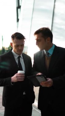 İki genç Avrupa işadamları bir anlaşma var ve iletişim. İlk tablet Pc ikinci kahve ile teklif verme ile yaptığı sunum reddetme. Parlak iş merkezi arka plan bina. Deniz mavisi ve