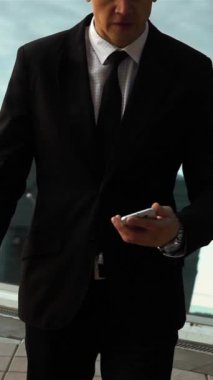 Ağır çekim. Akıllı telefondaki dehşet mesajları. Genç işadamı anlaşmayı bozdu. Teal ve turuncu stil. Arka planda cam iş merkezi var. Orta Dji Ronin saldırısı. Dikey Çekim.