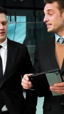 Ağır çekim: Tabletpc internet hizmeti veren iki beyaz yönetici. BG 'deki cam iş merkezi. deniz mavisi ve turuncu. Dikey Çekim.