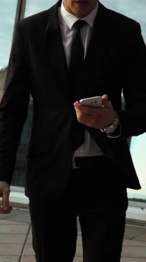 Ağır çekim. Akıllı telefondaki dehşet mesajları. Genç iş adamı Teal ve turuncu tarzı anlaşmayı bozdu. Arka planda parlak metalik iş merkezi var. Orta sabit kamera görüntüsü. Dikey Çekim.