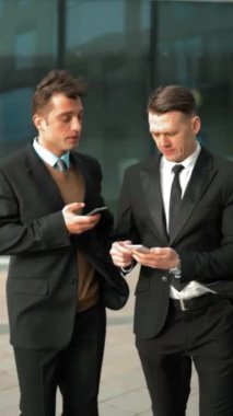 İki genç başarılı işadamları mobil akıllı telefonlar ile iletişim. Ofis binaları arka plan, iletişim kavramı ile bilgi alışverişini başvurun. Cam iş merkezi bölgesi. Tealand