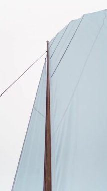 Ahşap yelkenli beyaz yelkenli, halatlar ve tahta bloklar. Sessiz sessiz gölün arka planı. Beyaz Tablo Dikey Çekim.