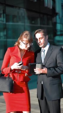 Genç işadamı tabletle kahverengi saçlı, kırmızı elbiseli çekici iş kadınına bir teklif yapıyor. El sıkışalım. Parlak bölge geniş açılı çekim. Güneşli Gün Dikey Vuruşu.