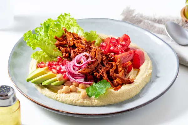Hummus with vegan meat in barbecue sauce, tomato and avocado salad. A healthy bowl