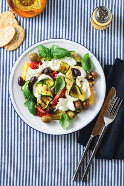 Akdeniz salatası, mozarella, zeytin, fesleğen ve ızgara sebze ile mavi çizgili keten masa örtüsü.