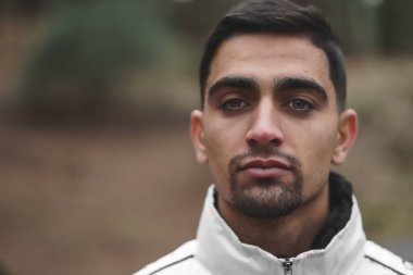 Ormanın ortasında siyah saçlı ve açık renk gözlü bir çocuğun portresi.