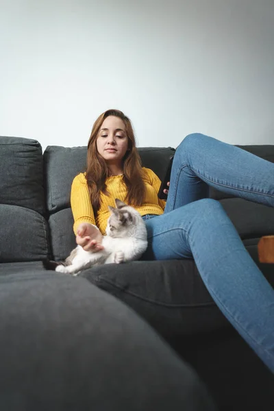 Kahverengi saçlı, sarı gömlekli, kot giyen, koltukta oturan, cep telefonu kullanan bir kadın..