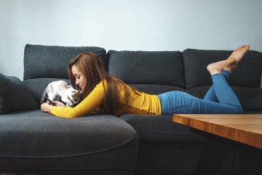 Sarı ceketli kadın kanepede beyaz kediyle oynuyor.