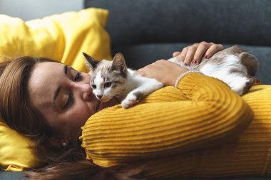 Sarı gömlekli kadın kanepede beyaz kediyle oynuyor.