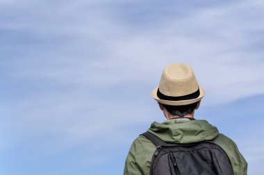 Mavi gökyüzüne karşı sırt çantalı bir gezginin arka görüntüsü. Turist, şapkalı gezgin gökyüzüne bakıyor..