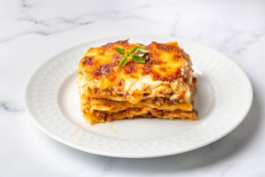 Portion of ground beef lasagna topped with melted cheese and garnished with fresh parsley served on a plate in close view for a menu