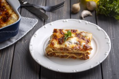 Portion of ground beef lasagna topped with melted cheese and garnished with fresh parsley served on a plate in close view for a menu