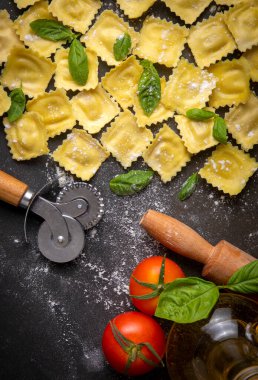 Delicious raw ravioli with flour and basil on dark background. The process of making Italian ravioli.