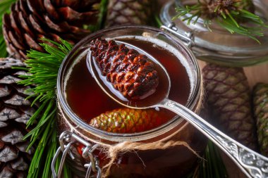 Genç kozalaklar tahta tahtadaki cam kasede sıkışıyor. Küçük kozalaklı lezzetli reçel.