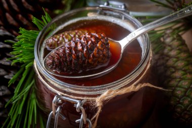 Genç kozalaklar tahta tahtadaki cam kasede sıkışıyor. Küçük kozalaklı lezzetli reçel.