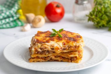 Portion of ground beef lasagna topped with melted cheese and garnished with fresh parsley served on a plate in close view for a menu