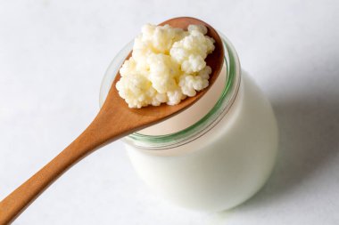 Kefir, kefir taneli mayalanmış süt içeceği. Ev yapımı kefir bir bardakta duruyor, kefir taneleri ve sütün yanında.