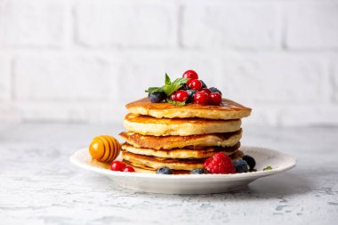 Sağlıklı yaz kahvaltısı, ev yapımı klasik Amerikan krepleri taze meyve ve bal, sabah açık gri taş arka plan fotokopi alanı üst görünüm