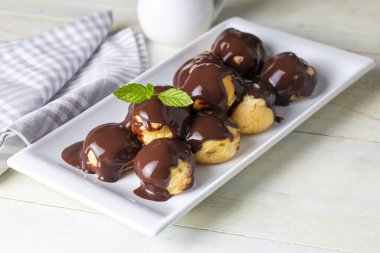 Çikolatalı ve beyaz tabaklı lezzetli profiteroller. Işık arkaplanı üzerine seçmeli odak resmi.