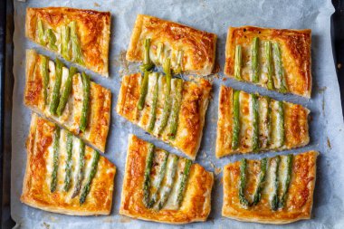 Baked green asparagus with ham and cheese in puff pastry sprinkled with sesame seeds and green basil leaves. 