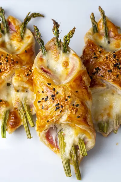 Baked green asparagus with ham and cheese in puff pastry sprinkled with sesame seeds and green basil leaves. 