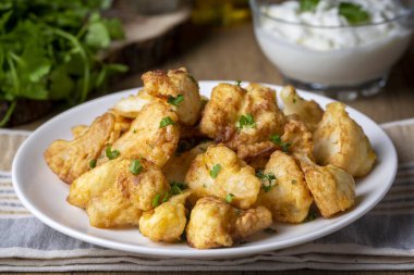 Fried in batter Cauliflower florets served on a black plate on a grey concrete table with ingredients, view from above, close-up, flatlay, copy space (Turkish name; karnabahar kizartmasi)