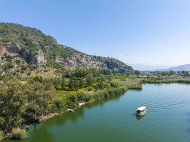 Dalyan - Mugla - Türkiye, 22 Ekim 2021, Dalyan, Mugla, Türkiye 'deki Kaunos antik kentinin kaya kesimli tapınak mezarları. Feribot ve arka planda oyulmuş mezarlarla güzel Dalyan nehir manzarası.