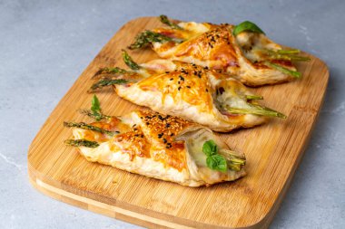 Jambon ve peynirli fırında yeşil kuşkonmaz üzerine susam tohumları serpiştirilmiş börek.