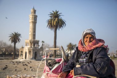 İzmir - Türkiye, 24 Ocak 2023, Konak Meydanı, saat kulesinin önünde kuşları besleyen kadın