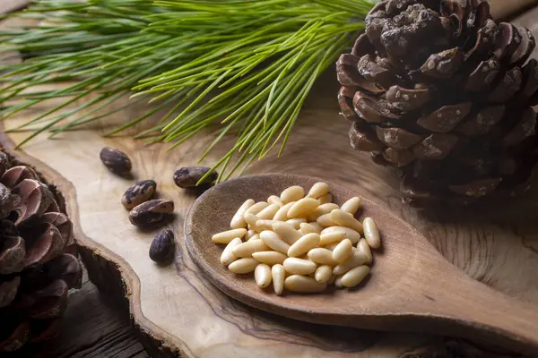 Pine nuts in the spoon and pine nut cone on the wooden table. Organic food.