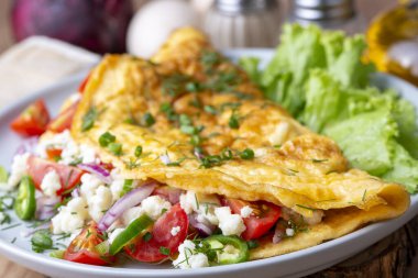 Homemade stuffed omelet on a plate. Egg omelet stuffed with fresh tomatoes, cheese and green parsley. Healthy vegetarian breakfast recipe.