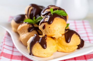 Çikolatalı ve beyaz tabaklı lezzetli profiteroller. Işık arkaplanı üzerine seçmeli odak resmi.