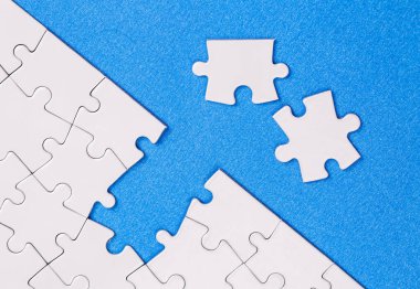 Missing jigsaw puzzle pieces. Business concept. Fragment of a folded white jigsaw puzzle and a pile of uncombed puzzle elements against