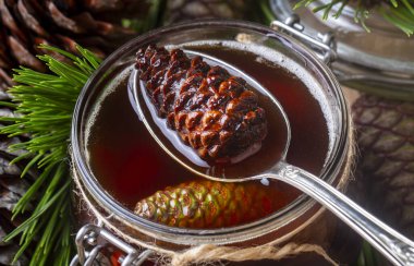 Genç kozalaklar tahta tahtadaki cam kasede sıkışıyor. Küçük kozalaklı lezzetli reçel.