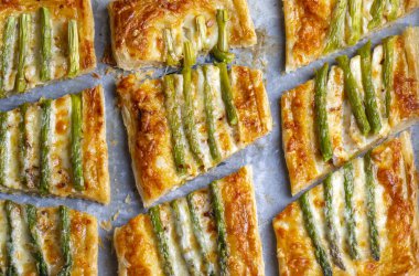 Baked green asparagus with ham and cheese in puff pastry sprinkled with sesame seeds and green basil leaves. 