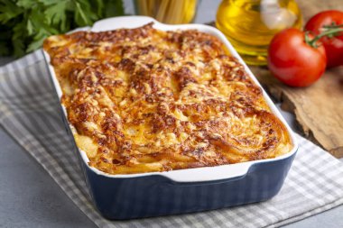 Eritilmiş mozzarella peyniri ile kaplı makarna güveç sosu ve bir masada beyaz bir fırın kabında servis edilir (Türk adı; firinda makarna veya firin makarna)