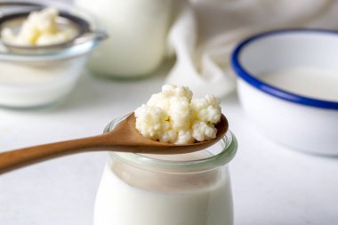 Kefir, kefir taneli mayalanmış süt içeceği. Ev yapımı kefir bir bardakta duruyor, kefir taneleri ve sütün yanında.