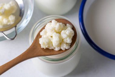 Kefir, kefir taneli mayalanmış süt içeceği. Ev yapımı kefir bir bardakta duruyor, kefir taneleri ve sütün yanında.