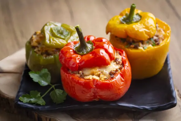Stuffed peppers, halves of peppers stuffed with rice, dried tomatoes, herbs and cheese in a baking dish on a blue wooden table, top view. (Turkish name; biber dolmasi)