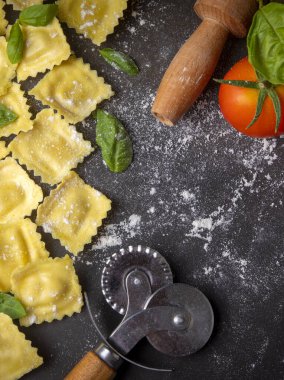 Delicious raw ravioli with flour and basil on dark background. The process of making Italian ravioli.