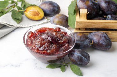 Mavi seramik kasede ev yapımı erik reçeli ve beyaz ahşap arka planda böğürtlen..