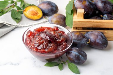 Mavi seramik kasede ev yapımı erik reçeli ve beyaz ahşap arka planda böğürtlen..