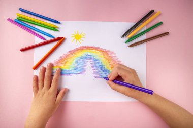 Çocuk elleri boyuyor gökkuşağını boyuyor pastel boyalarla.