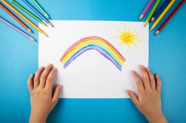 Çocuk elleri boyuyor gökkuşağını boyuyor pastel boyalarla.