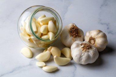 Cam bir kasede sarımsaklı karanfil ve beyaz ahşap bir masada soyulmuş sarımsak..